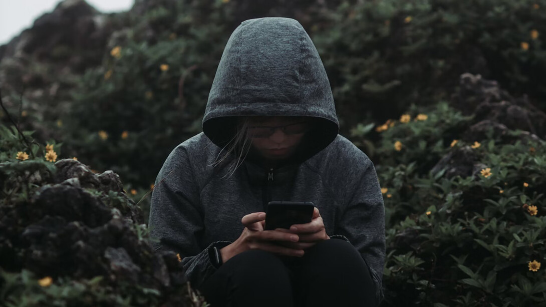 A person sitting on a rock, staring at their phone, surrounded by a sense of grief and the haunting presence of technology