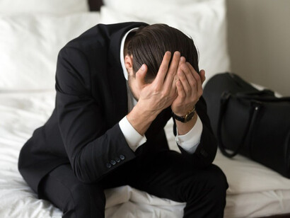 A man sits on his bed, overwhelmed and holding his head, battling through his challenges