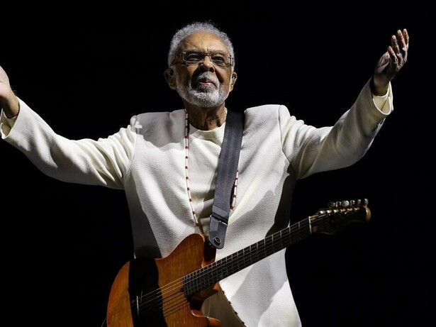 Gilberto Gil no palco, durante a turnê Tempo Rei, no Mineirão, em 2025, com os braços abertos, a guitarra presa ao corpo e um fundo completamente escuro. De braços abertos diante do público, o artista parece acolher as muitas histórias e gerações que sua música acompanhou ao longo de mais de seis décadas de carreira. Do primeiro LP Realce ouvido aos 10 anos ao show de despedida dos grandes palcos, sua música atravessou décadas e se misturou às memórias de uma vida. Sob a luz do palco, a imagem parece traduzir o próprio espírito da canção: o tempo passa, transforma as formas do viver e, ainda assim, algumas músicas permanecem