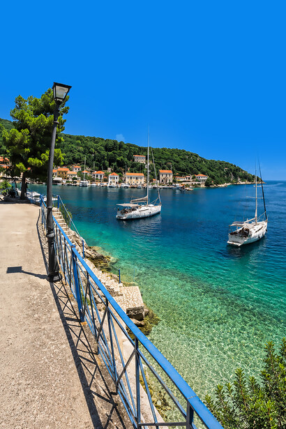 A scenic view of Kioni Village on Ithaca Island, Greece, featuring crystal-clear blue waters, traditional houses, and boats moored along the picturesque harbor