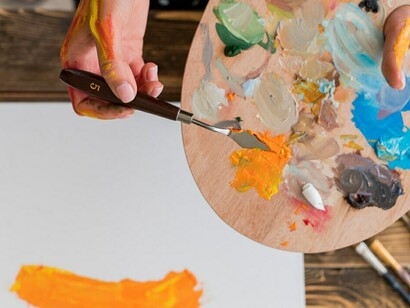 From above, an artist uses their hands to apply colors to the canvas, highlighting the hands-on approach to the creative process