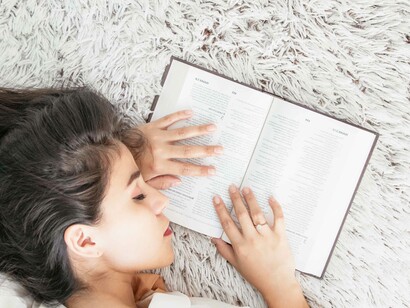 A woman falling asleep to an open textbook seeking rest from all the hard work and dreaming a dream that's placing her at ease