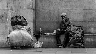 A homeless man sits against a city wall, highlighting the realities of poverty and economic inequality