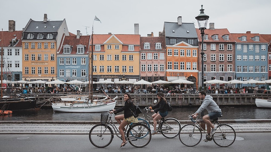 On Copenhagen's latest bridge, three cyclists share a vibrant pathway beneath a clear white and blue sky, surrounded by urban buildings