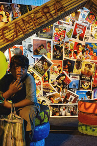 A child sits with balloons in front of a wall of movie posters, Kolkata, WB, India

