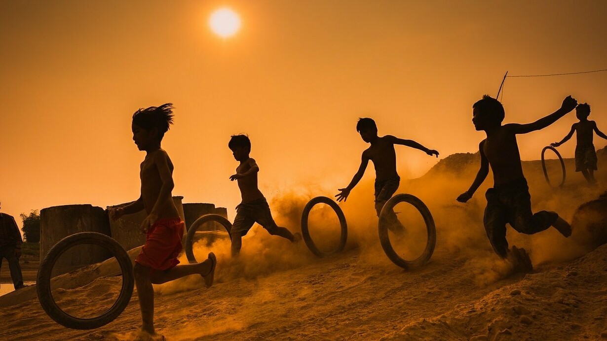 Dei bambini corrono sulla sabbia giocando con ruote di gomma