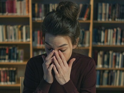 A tired woman sitting at a desk, rubbing her eyes from exhaustion, illustrating the toll of overwork and the pressures many face, leaving little time for leisure or mental well-being