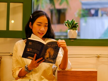 A woman quietly reading a book in a peaceful space, representing the value of setting aside personal time for self-care