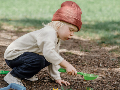 A little boy plays in the backyard with a plastic shovel, digging for hidden treasure beneath the soil