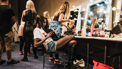 The vibrant energy of the backstage preparation area at a fashion show, where models, designers, and stylists collaborate in a flurry of activity to create stunning runway looks