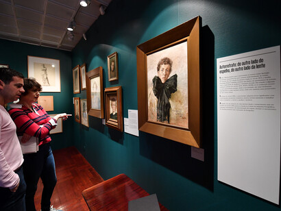 Duas pessoas contemplam um retrato da exposição. Núcleo Casa Museu Marta Ortigão Sampaio, CMP. Fotografia de Miguel Nogueira