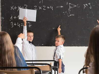 Schoolchildren are seated in the classroom, engaged in a lesson in front of the blackboard