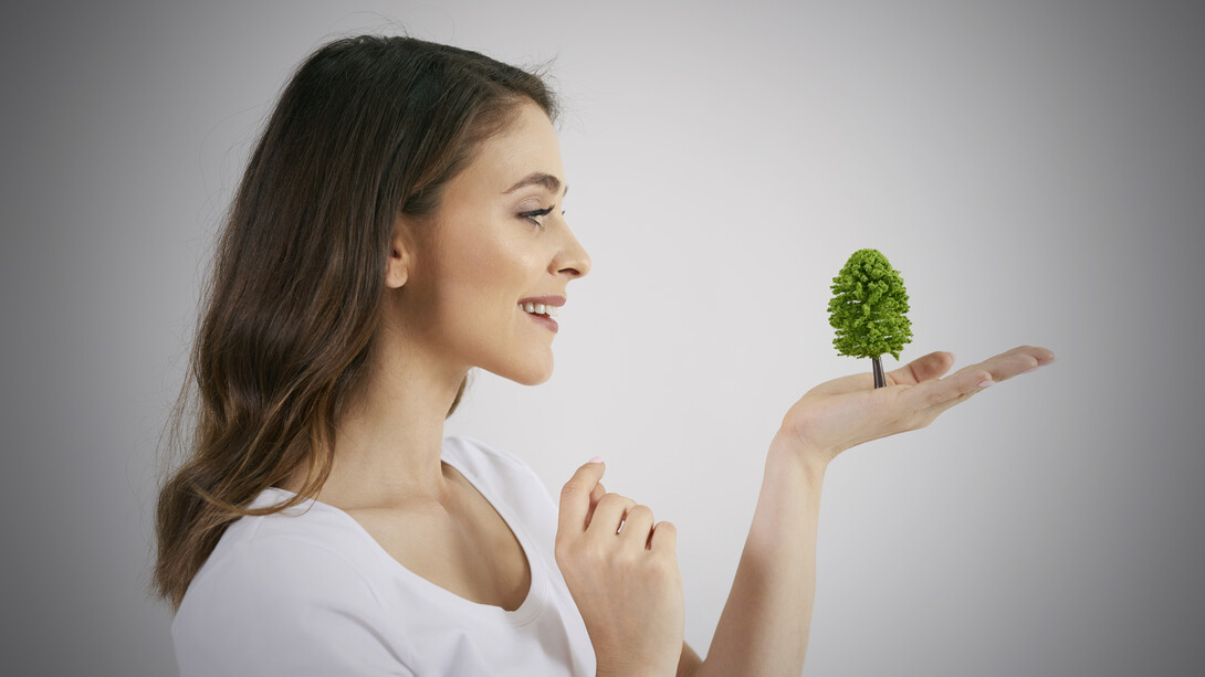 A woman gently holds a growing tree in her hand, symbolizing care for nature and growth