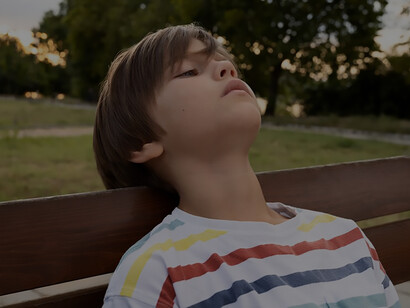 A melancholic scene through a medium shot, depicting a thoughtful boy sitting on a bench, immersed in nostalgic daydreams of childhood
