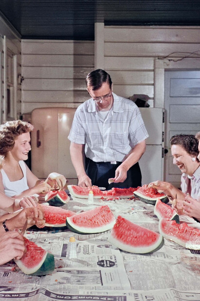 Margaret Bourke-White, Una famiglia condivide una risata mentre taglia fette di anguria su un tavolo da cucina coperto di giornali. La foto è stata scattata per un servizio di fotogiornalismo, intitolato “Separate and Unequal”, sulla disuguaglianza razziale e le strutture segregate a Greenville. Greenville, Carolina del Sud, 1956. Per gentile concessione di Margaret Bourke-White/The Life Picture Collection/Shutterstock