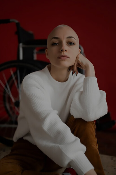 With unwavering strength, a woman battling cancer exudes positivity while posing next to her wheelchair, symbolizing her resilience and optimistic spirit in the face of adversity