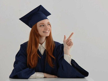A young female university graduate wearing an academic cap, sitting at a table, smiling and posing for a photo