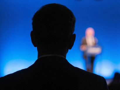 A silhouette of a man in a conference setting, listening attentively