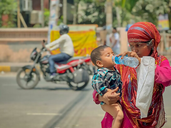 An Indian man gives his child water to stay hydrated during extreme summer heat, highlighting the risks of dehydration and heat exhaustio