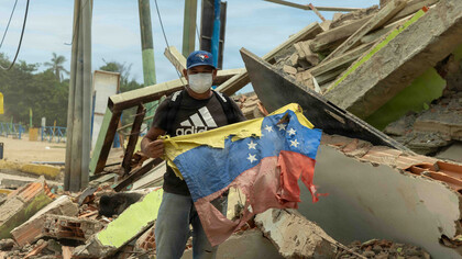 Ciudadano venezolano sostiene una bandera nacional junto a su restaurante dañado tras un terremoto en La Guaira, Venezuela, como signo de resiliencia. 28 de junio de 2026