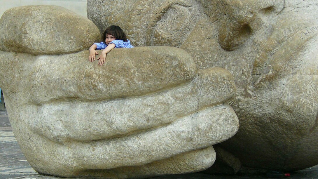 A child sits inside the giant hand of a face statue