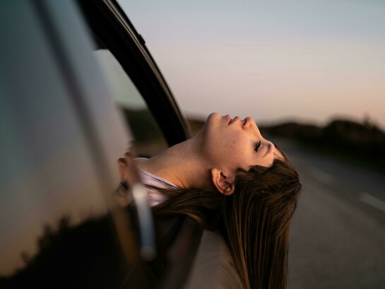 A woman leans out of a car window, enjoying the fresh air