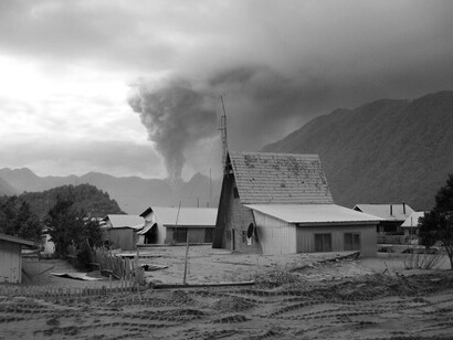 La ceniza volcánica cubre calles y terrenos de Chaitén mientras, al fondo, una columna de humo emerge del volcán