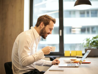 A businessman drinking coffee and smiling while on a conference call