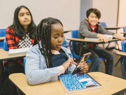 A young girl in the classroom, attentively gazing at her smartphone