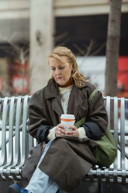 Melancholic woman sitting alone on a city bench, holding a takeaway coffee as the urban world moves around her