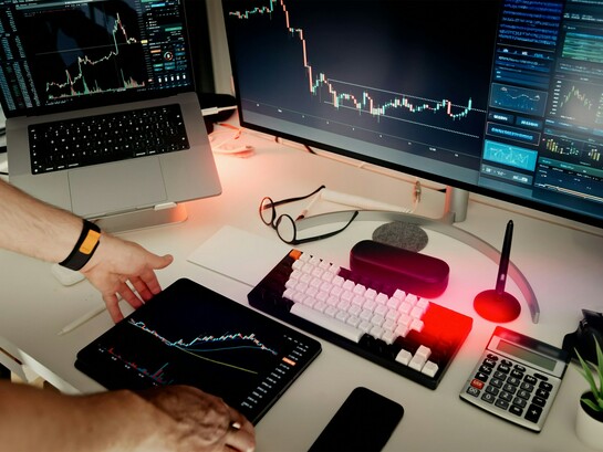 Un grand moniteur principal et un ordinateur portable surélevé présentent des courbes de tendance et des données de marché lumineuses