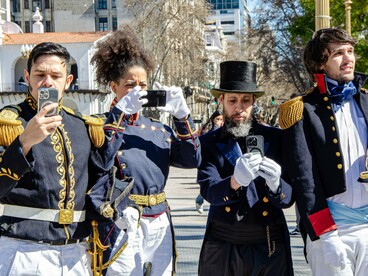 Pessoas vestidas com uniformes históricos utilizam smartphones durante uma reconstituição em Buenos Aires, aproximando a representação do passado dos meios digitais contemporâneos. Na Argentina, a campanha de Javier Milei em 2023 demonstrou a força de vídeos virais, memes e influenciadores na disputa política, em um ambiente marcado pela insatisfação popular com a crise econômica e pela retórica antissistema