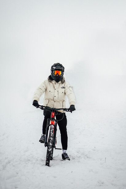 Riding a red mountain bike, a man in a beige jacket pedals through the snow-covered landscape of Jammu & Kashmir, India, under the bright daylight