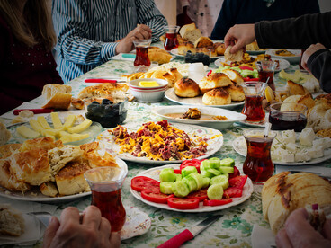 A Turkish family shares a traditional breakfast, surrounded by an abundant selection of breads, cheeses, olives, fresh vegetables, and tea