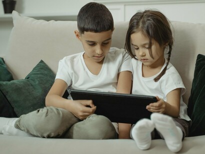 Um menino e uma menina observam atentamente o conteúdo exibido em um tablet, compartilhando a experiência diante da tela. O contato com as tecnologias digitais começa cada vez mais cedo e passa a integrar as formas pelas quais crianças descobrem informações, histórias e novos conhecimentos