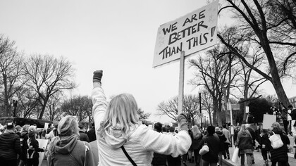 A woman seen from behind holding a sign with a hopeful message at a demonstration