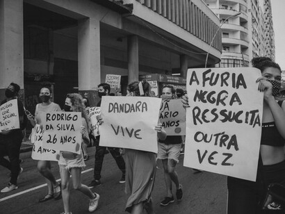 Manifestantes carregam cartazes com frases como "A fúria negra ressuscita outra vez" (essa é uma das frases mais emblemáticas do rap brasileiro; ela faz parte da música "Capítulo 4, Versículo 3", lançada em 1997 pelos Racionais MC's no clássico álbum "Sobrevivendo no Inferno"); "Dandara vive" (Dandara dos Palmares foi uma grande liderança feminina e guerreira do Quilombo dos Palmares, no Brasil colonial. Companheira de Zumbi dos Palmares, ela dominava técnicas de capoeira, lutava na linha de frente contra as tropas portuguesas e ajudava a criar estratégias de resistência); e "Rodrigo da Silva 26 anos" (homem negro, trabalhava como garçom, foi assassinado pela Polícia Militar do Rio de Janeiro enquanto esperava sua esposa e filhos retornarem para casa, em um dia chuvoso, quando ele os aguardava com um guarda-chuva que foi confundido com um fuzil por policiais que atiraram contra ele, conforme relato de testemunhas). O artigo destaca a importância das mobilizações sociais contra diferentes formas de exclusão e violência
