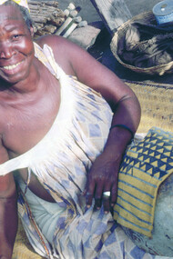 Ill. 1. Tonguoy Diarra pausing during the painting of the sleeve of a man’s tunic. The sleeve bearing the “Piece of a gourd” (Filen koloni) pattern is stretched across an empty calabash. Dyers always use the calabash as a support because it enables them to hold the metal spatula vertical to the cloth and to work on very small areas without staining other sections of the design. Kolokani.  
Photocredit Sarah C. Brett–Smith  
