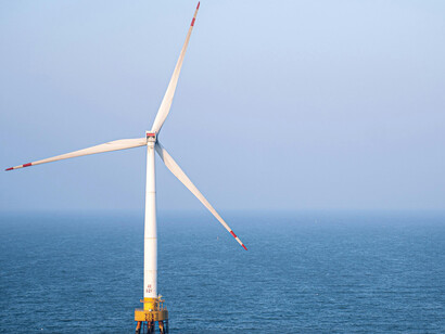 A lone wind turbine standing in calm ocean waters