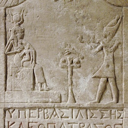 Un’iscrizione votiva dedicata dal greco Onnophris, che raffigura un faraone maschio nell’atto di presentare offerte alla dea Iside, ma che nel testo rende onore a una regina Cleopatra (probabilmente Cleopatra VII). Conservata al Louvre, Parigi, Francia