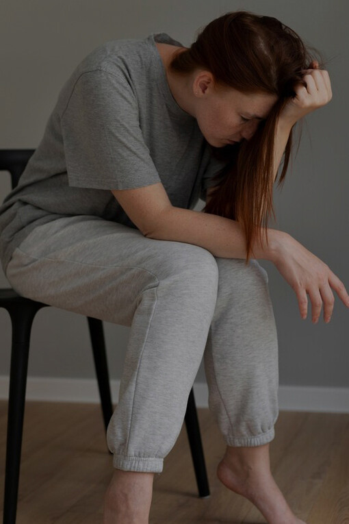 Seated on a chair, a woman appears lost in thought, burdened by feelings of sadness and worry