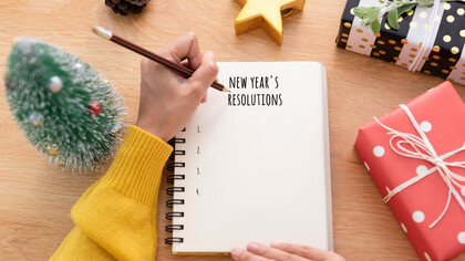 Woman hand writing New years resolution on note paper on new year day