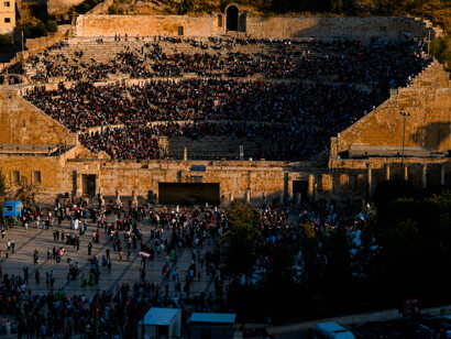 People filling a historic Roman theatre at sunset, capturing the lively energy of a cultural event in an ancient open-air setting