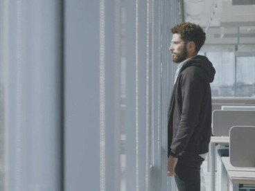 In a moment of silence, looking out from the office window, the weight of unspoken pain and unseen struggles becomes painfully clear on this man's face