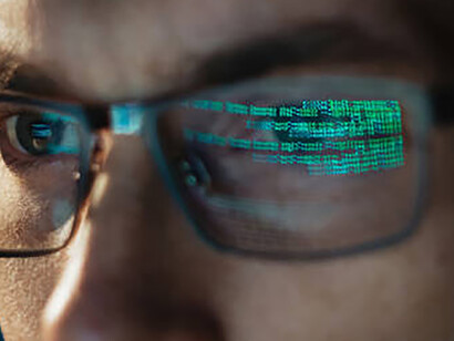 In the age dominated by digitalism, a young businessman's contemplation of a computer screen is mirrored in his glasses, symbolizing the integration of technology into all aspects of contemporary existence