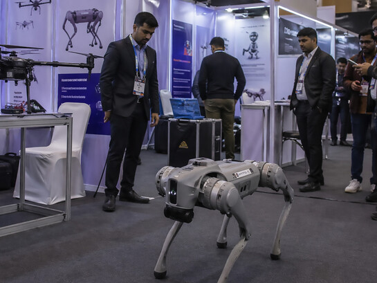 A robotics demonstration at a crowded technology exhibition, where a quadruped robot and surrounding displays highlight the fine line between innovation, presentation, and perception in modern AI showcases