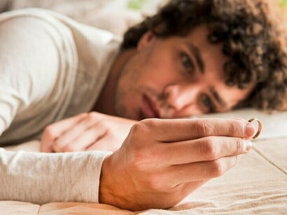A blurred man holds a wedding ring in his hand, while a sad couple sits in the background, surrounded by loneliness and despair