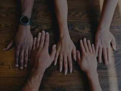 Five hands placed down on a table to mark the bond and unity of their team as each hand represents a different race or gender