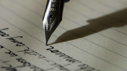 A sleek fountain pen glides across the black lined paper, leaving behind elegant strokes of ink