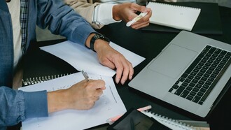 People working on laptops and paper to complete university work 